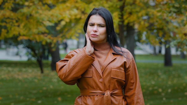 Young hispanic woman standing outdoors feeling toothache holding hand on cheek jaw has dental