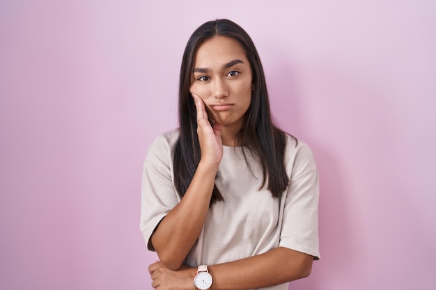 Young hispanic woman standing over pink background thinking looking tired and bored with depression problems with crossed arms.