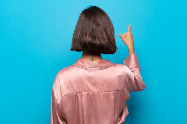 Photo young hispanic woman standing and pointing to object on copy space, rear view