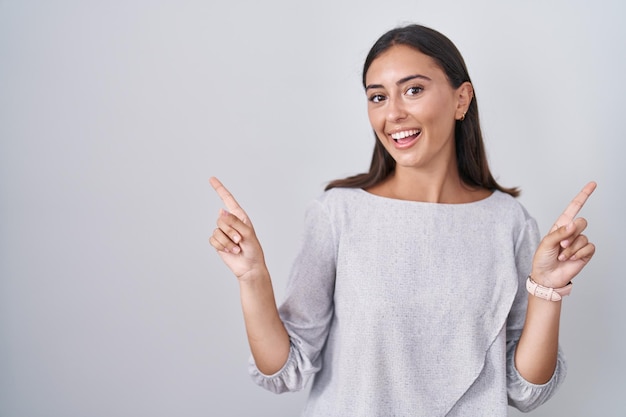 Young hispanic woman standing over white background smiling confident pointing with fingers to different directions. copy space for advertisement