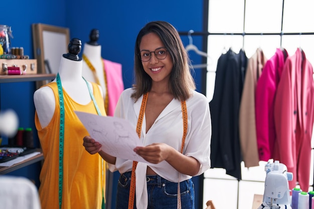 Young hispanic woman tailor reading document at sewing studio