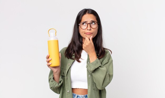 Young hispanic woman thinking, feeling doubtful and confused and holding a coffee thermos