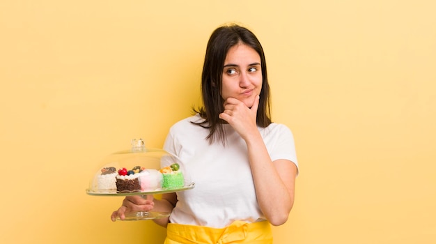 Young hispanic woman thinking feeling doubtful and confused home made cakes concept