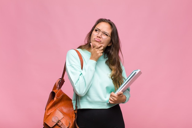 ヒスパニック系の若い女性が考え、疑わしく混乱し、さまざまな選択肢があり、どの決定を下すか疑問に思っています