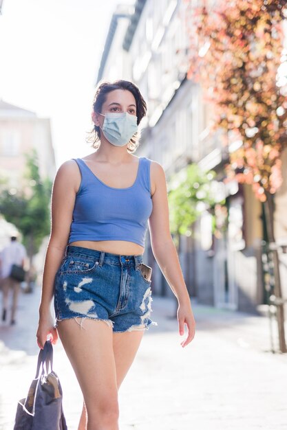Young hispanic woman walk in the city shopping urban casual with face mask