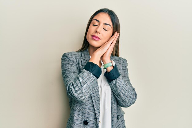 Young hispanic woman wearing business clothes sleeping tired dreaming and posing with hands together while smiling with closed eyes.