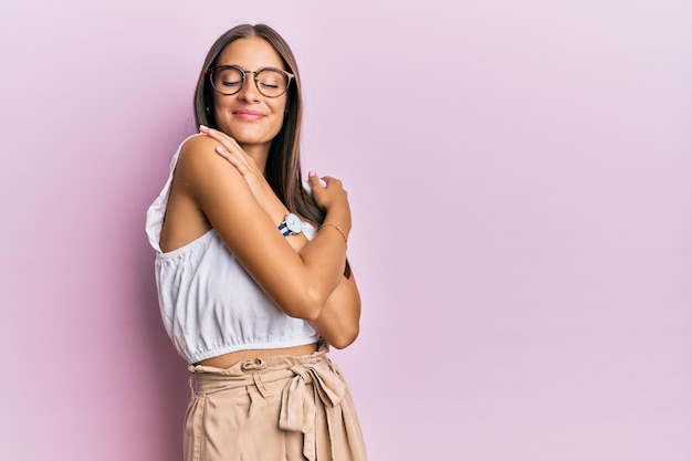 Young hispanic woman wearing casual clothes and glasses hugging oneself happy and positive smiling confident self love and self care