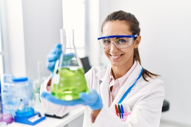 Foto giovane donna ispanica che indossa l'uniforme dello scienziato che tiene la provetta in laboratorio