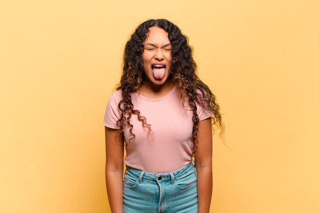 Young hispanic woman with cheerful, carefree, rebellious attitude, joking and sticking tongue out, having fun