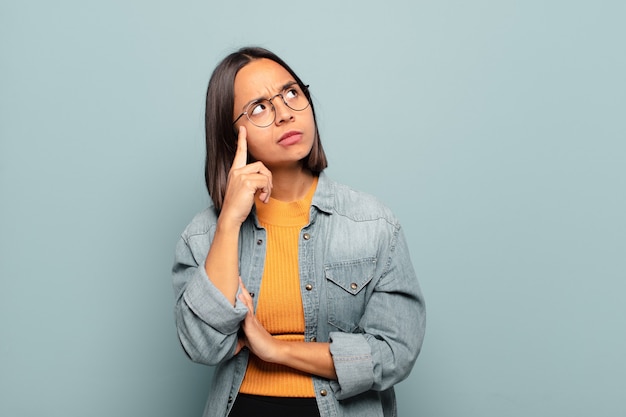 Young hispanic woman with a concentrated look, wondering with a doubtful expression, looking up and to the side