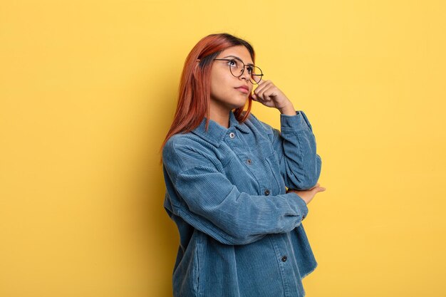 Young hispanic woman with a concentrated look, wondering with a doubtful expression, looking up and to the side