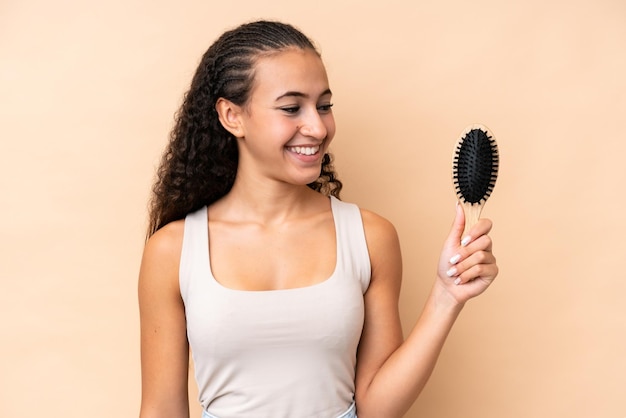 Young hispanic woman with hair comb isolated on beige background with happy expression