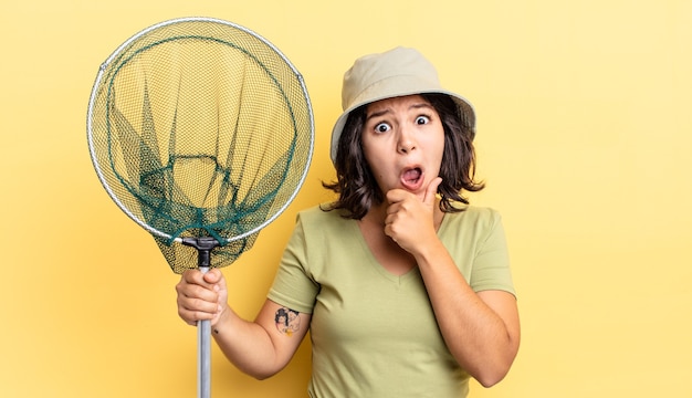 Young hispanic woman with mouth and eyes wide open and hand on chin. fisher net concept