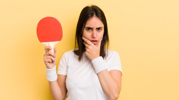 Young hispanic woman with mouth and eyes wide open and hand on chin ping pong concept