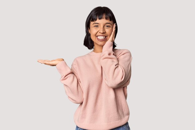 Young Hispanic woman with short black hair in studio holds copy space on a palm