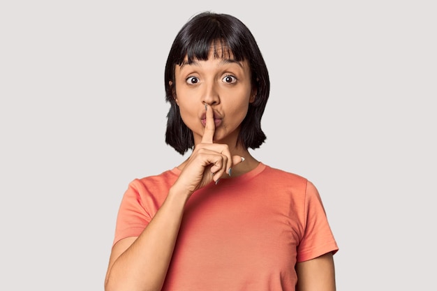 Young Hispanic woman with short black hair in studio keeping a secret or asking for silence