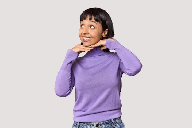 Young Hispanic woman with short black hair in studio keeps hands under chin is looking happily aside