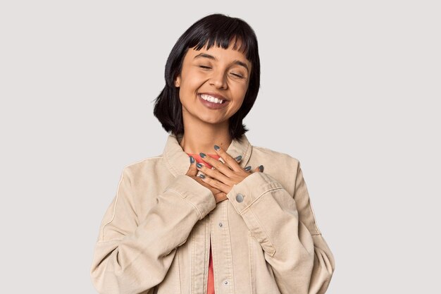 Photo young hispanic woman with short black hair in studio laughing keeping hands on heart concept