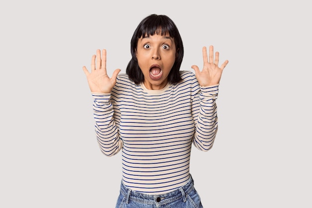 Young Hispanic woman with short black hair in studio receiving a pleasant surprise excited