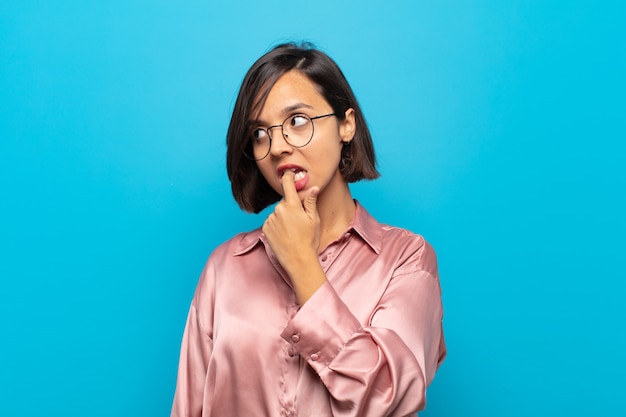 Young hispanic woman with surprised, nervous, worried or frightened look, looking to the side towards copy space