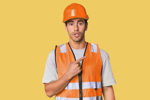 Young Hispanic worker in safety gear pointing to the side