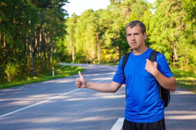 Young hitchhiking traveler try to stop car on forest road