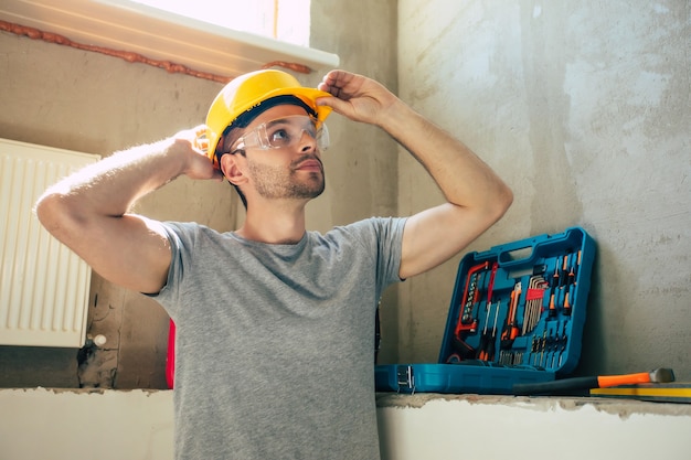 Young home repair male or worker busy with house renovation, holds building equipment, wears casual working clothes in the new build