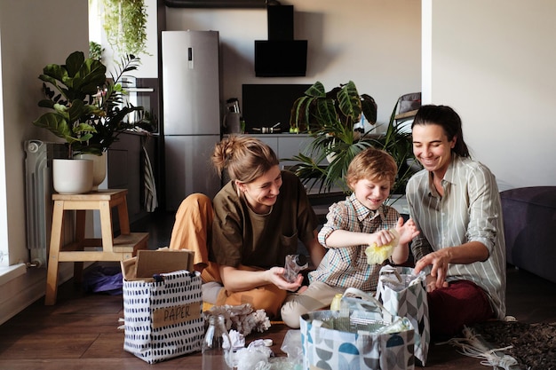 Young homosexual mothers teaching their son to separate rubbish in different bags for recycling