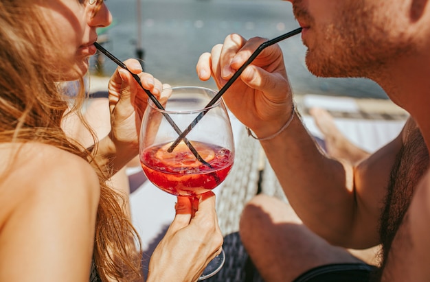 Young hot couple resting at swimpool, sharing cocktail