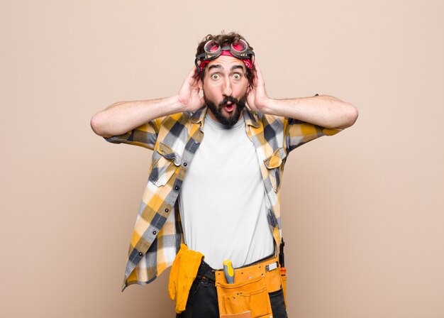 Young housekeeper man looking excited and surprised, open-mouthed with both hands on head, feeling like a lucky winner over wall