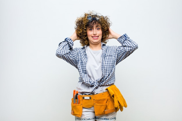 Young housekeeper woman feeling stressed, worried, anxious or scared, with hands on head, panicking at mistake against white wall