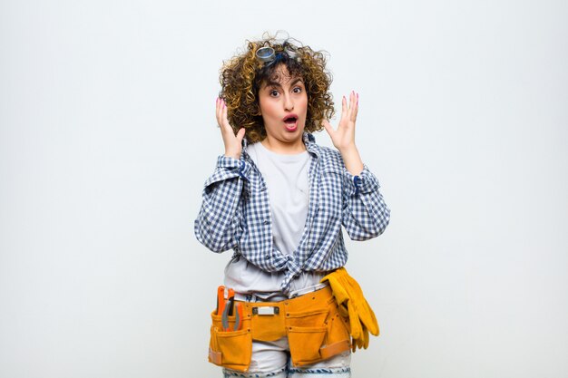 Young housekeeper woman looking shocked and astonished, with jaw dropped in surprise when realizing something unbelievable over white wall