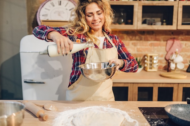 Young housewife in an apron pours milk in a bowl