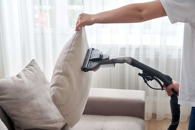 Young housewife Cleaning Sofa with Vacuum Cleaner in living room