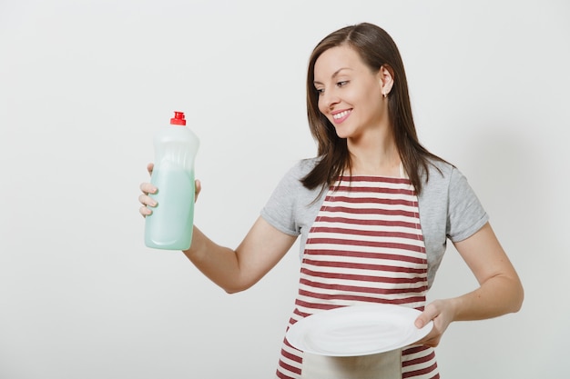 Young housewife in striped apron isolated. Housekeeper woman holds bottle with cleaner liquid for washing dishes, white empty round plate