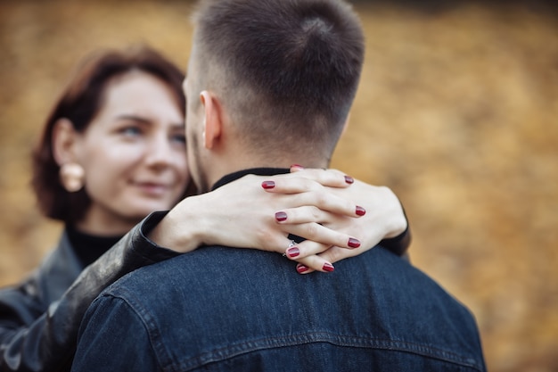 Photo young hugging couple of lovers on a blurry background of fallen autumn leaves in the park. romantic, love concept