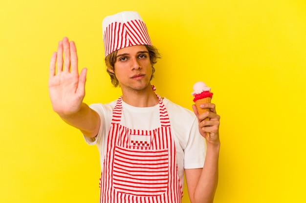 노란색 배경에 격리된 아이스크림을 들고 화장을 한 젊은 아이스크림 제작자는 손을 뻗은 채 정지 신호를 보여주며 당신을 방해합니다.