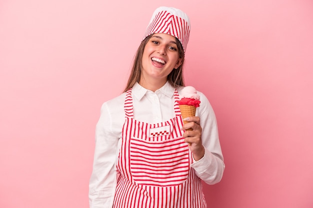 Giovane gelatiera donna che tiene il gelato isolato su sfondo rosa felice, sorridente e allegro.