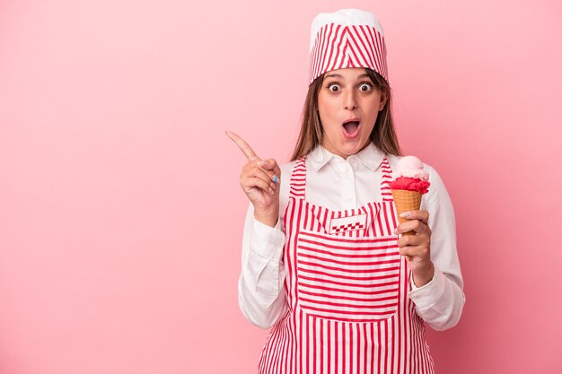 Young ice cream maker woman holding ice cream isolated on pink background pointing to the side