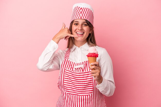 Young ice cream maker woman holding ice cream isolated on pink background showing a mobile phone call gesture with fingers.