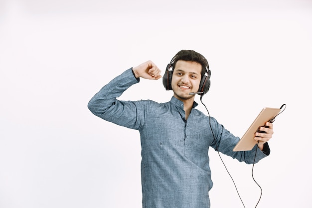 Giovane ragazzo indaiano in cuffie che ascolta la musica. ballando sul muro bianco, isolato.