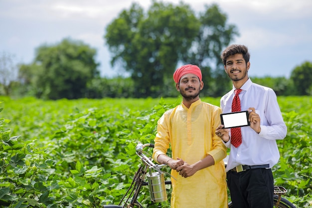 綿花畑で農民とスマートフォンを示す若いインドの農学者または銀行家