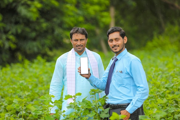 Giovane agronomo indiano o banchiere che mostra smartphone con gli agricoltori al campo agricolo.