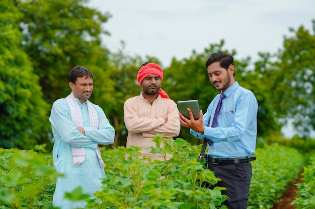 Young indian agronomist or banker showing some detail to farmer in tablet to farmers at agriculture field.