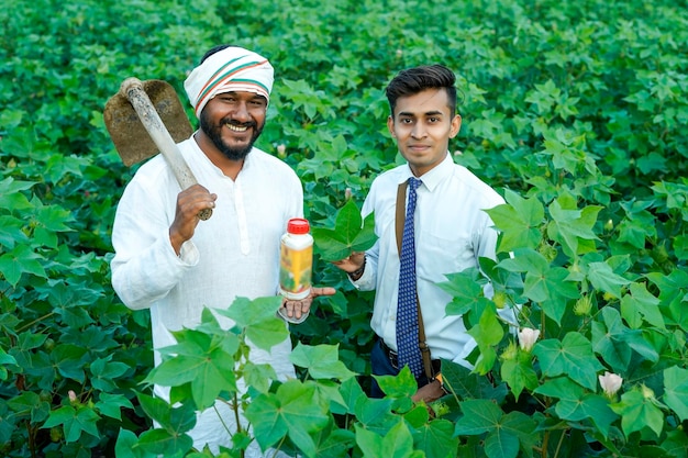 Foto giovane agronomista indiano che dà una bottiglia di fertilizzante liquido a un contadino in un campo di agricoltura verde