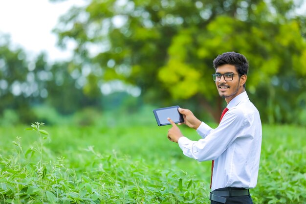 Young indian agronomist showing smartphone at field