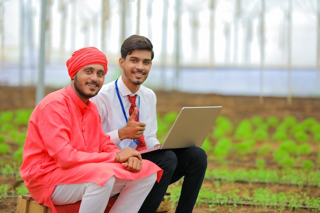 온실에서 노트북에 농부에게 몇 가지 정보를 보여주는 젊은 인도 농업 경제학자