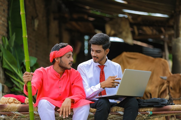 Young indian agronomist showing some information to farmer in laptop at home