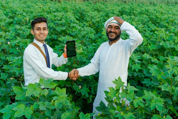 Young indian agronomist showing some information to farmer in tablet at agriculture field