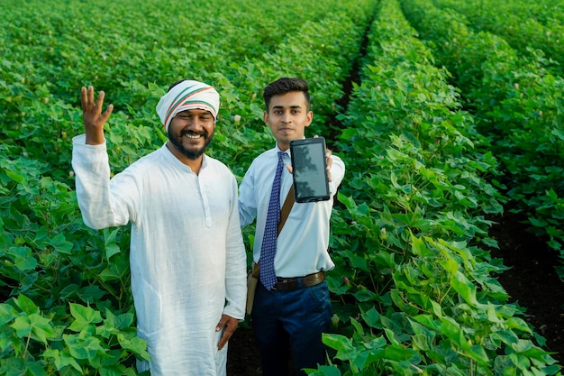 Foto un giovane agronomo indiano mostra alcune informazioni a un contadino su un tablet in un campo agricolo